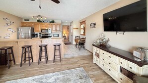 A modern kitchen with a bar area, wooden cabinets, a ceiling fan, and a flat-screen TV. - Loto fun at 21 Lakeview Condo (Osage Beach)