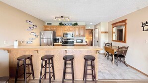 A kitchen with wooden cabinets, a central island with stools, a dining area with a table and chairs, and a mirror on the wall. - Loto fun at 21 Lakeview Condo (Osage Beach)
