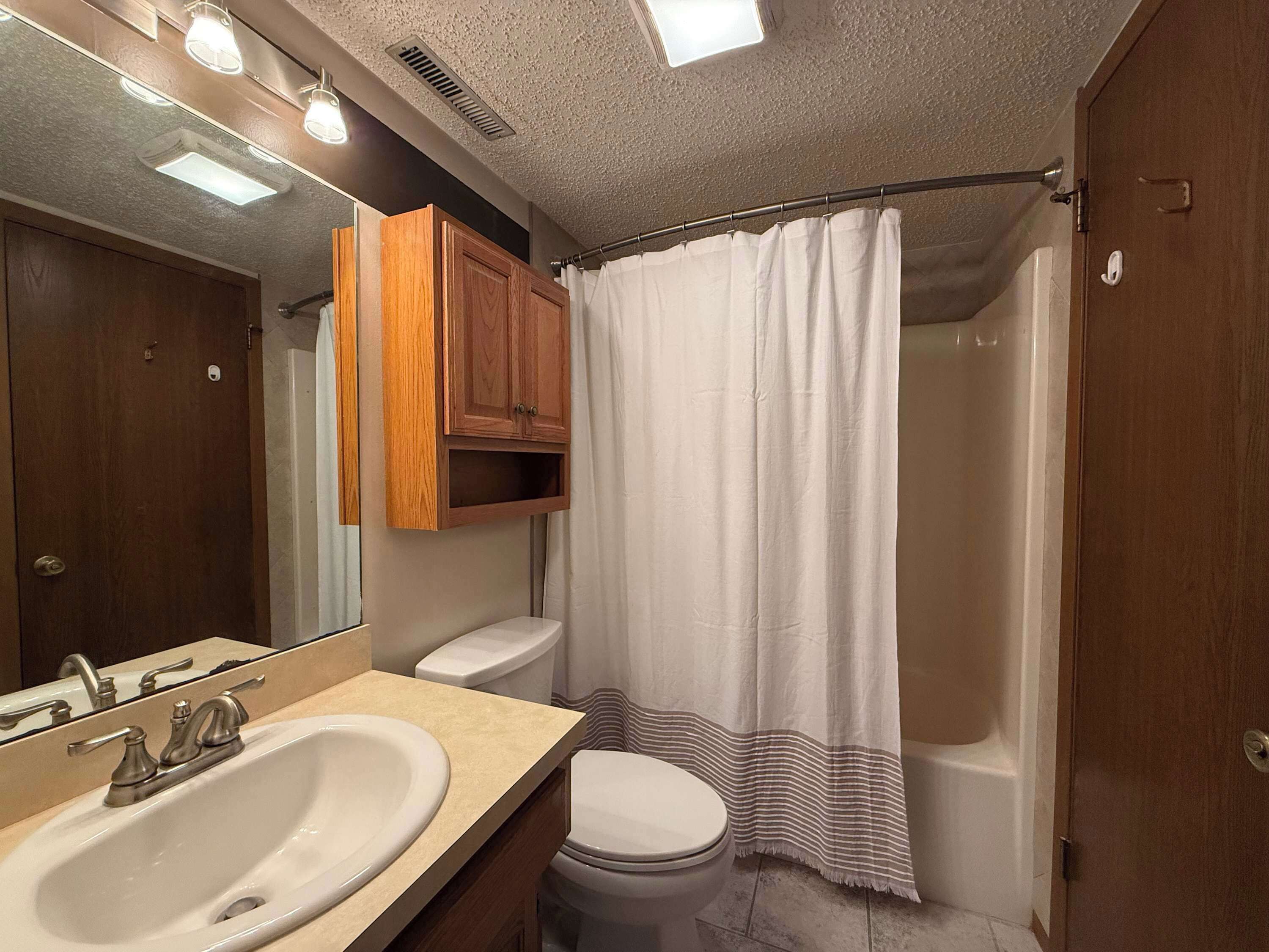 Une salle de bain équipée d’un lavabo, de toilettes, d’un rideau de douche et d’un meuble en bois.