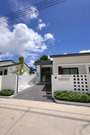A modern building with a gated entrance, a nameplate reading 'HOME GALLERY,' and a clear sky with clouds. - Coxy 2-bedroom house with AC in charming Near Bangtao Beach Phuket (Thalang District)