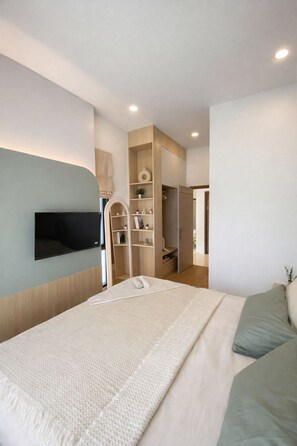 A modern bedroom with a bed, a TV mounted on the wall, built-in shelving, and a wardrobe. - Coxy 2-bedroom house with AC in charming Near Bangtao Beach Phuket (Thalang District)