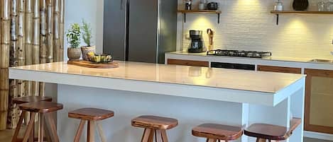 Una cocina con una isla central, lámparas colgantes de mimbre y taburetes de madera.