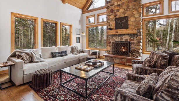 Un salon chaleureux avec une cheminée en pierre, de grandes fenêtres et un haut plafond en bois.