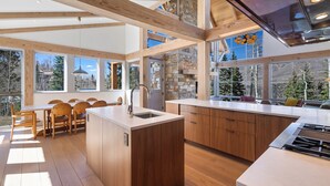A modern kitchen with wooden beams, large windows, and a dining area with chairs. - Ski In/Out, Hot tub, Sauna, Fireplaces, Fire Pit, Game Room (Mountain Village)