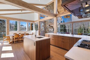 A modern kitchen with wooden beams, large windows, and a dining area with chairs. - Ski In/Out, Hot tub, Sauna, Fireplaces, Fire Pit, Game Room (Mountain Village)