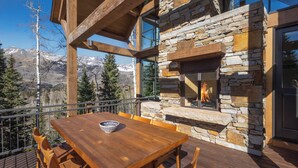 A wooden deck with a stone fireplace, a dining table, and chairs. - Ski In/Out, Hot tub, Sauna, Fireplaces, Fire Pit, Game Room (Mountain Village)