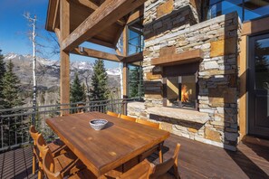 A wooden deck with a stone fireplace, a dining table, and chairs. - Ski In/Out, Hot tub, Sauna, Fireplaces, Fire Pit, Game Room (Mountain Village)