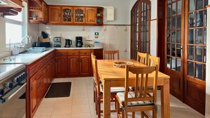 Een keuken met houten kastjes, een eettafel met stoelen, een fornuis en een groot raam met ruiten.