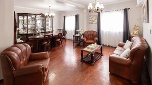 Een woonkamer met lederen banken, een salontafel, een eethoek met een glazen vitrine en een kroonluchter.