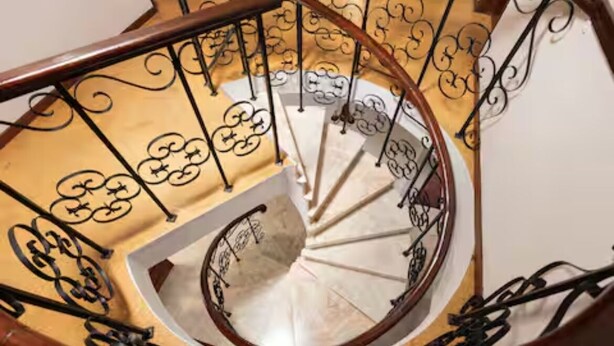 Een wenteltrap met sierlijke metalen leuningen en een houten handrail.