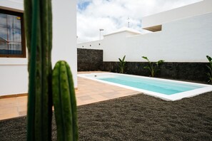 A modern outdoor pool area with a stone wall, a cactus, and a clear sky. - Villa Yaiza : Private pool + Garden : 3BR (Yaiza)