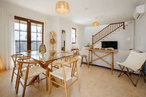 A modern living room with a glass dining table, wooden chairs, a sofa, a TV, and a staircase. - Villa Yaiza : Private pool + Garden : 3BR (Yaiza)