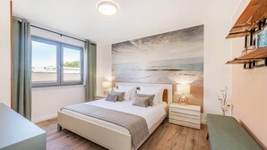 A bedroom with a bed, bedside tables, a bench, a window with curtains, and a wall with a painting. - Vacation apartment in Zinnowitz with terrace, WLAN & playground - ideal for families (Zinnowitz)