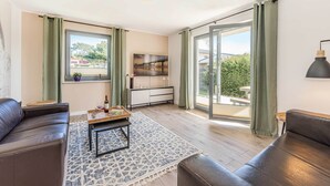 A living room with a sofa, coffee table, and a view of the outdoors through a sliding door. - Vacation apartment in Zinnowitz with terrace, WLAN & playground - ideal for families (Zinnowitz)