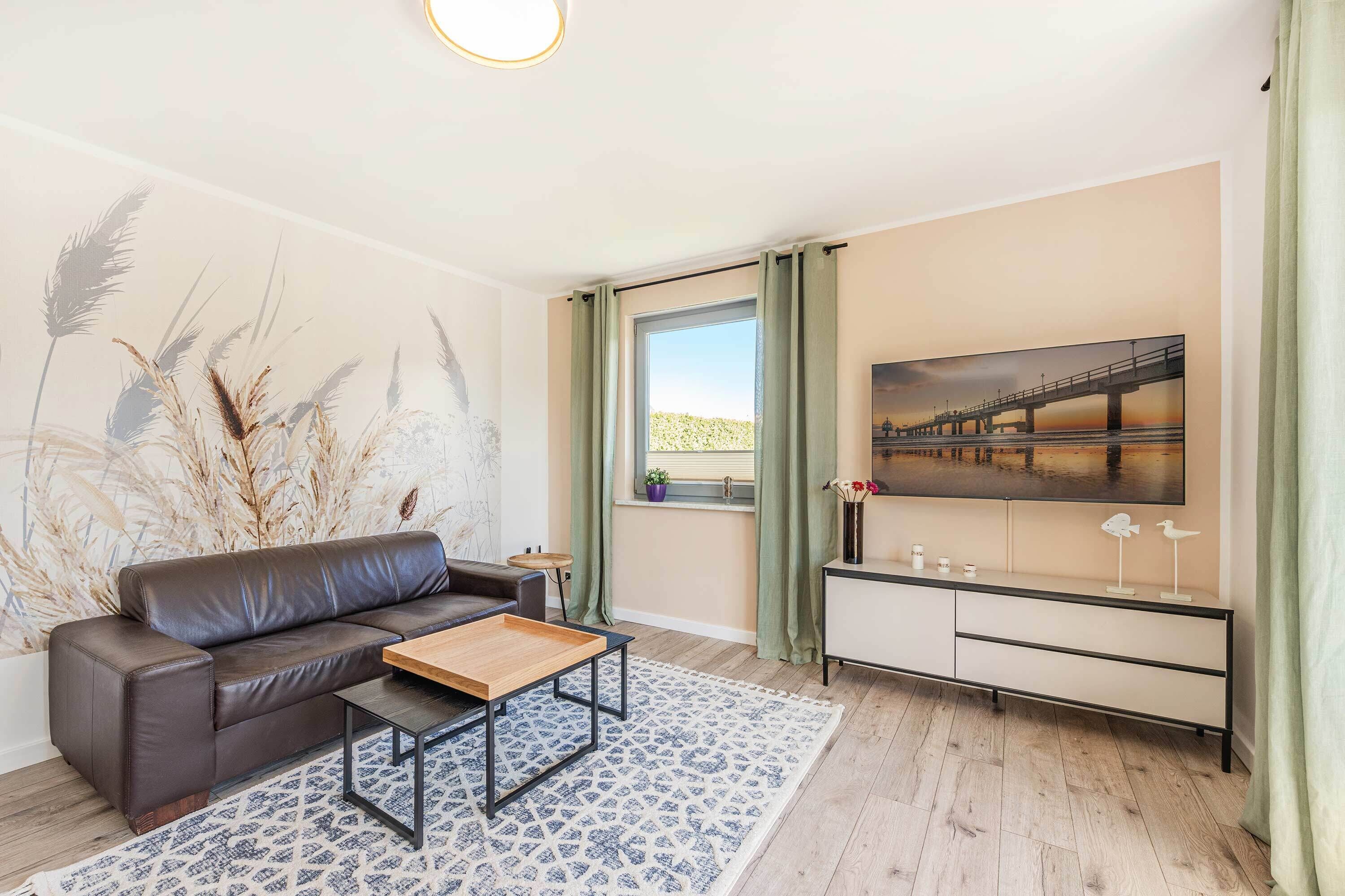Una sala de estar moderna con un sofá de cuero, una mesa de centro de madera, un tapete estampado, un televisor en la pared y una ventana con cortinas.
