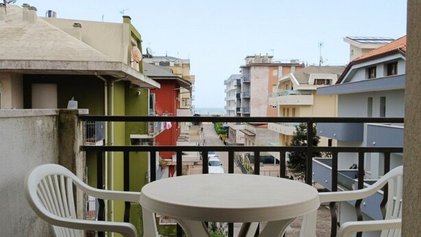 A balcony with a round table and two chairs, overlooking a residential area with buildings and a view of the sea. - RG006 - Bellaria, comfortable two-room apartment with sea view (Bellaria-Igea Marina)