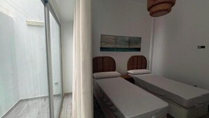 Una habitació amb dos llits, una porta de vidre que dona a un balcó i un quadre a la paret.