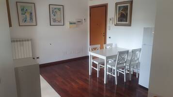 Une pièce avec une table et des chaises blanches, un radiateur, une porte et des œuvres d’art encadrées accrochées aux murs.