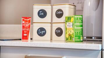 Vier gelabelde containers op een aanrecht: Thee, Koffie, Suiker en Melk.