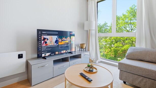 Una sala de estar moderna con una televisión de pantalla plana, un sofá, una mesa de centro y un ventanal con vistas a árboles.