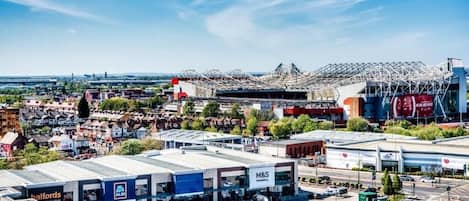 A commercial area with a large parking lot, a M&S store, and a stadium with a distinctive roof structure.