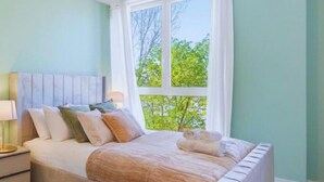 Un dormitorio con cama, mesita de noche, lámpara y ventana con vistas a árboles.
