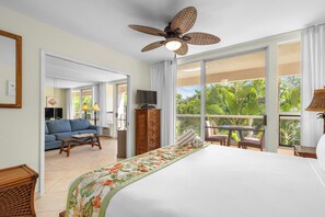 Ein Hotelzimmer mit Bett, Deckenventilator, Fernseher, Holzschrank, Sofa und Balkon mit Blick auf Grünflächen.