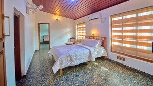 A bedroom with a bed, a ceiling fan, a window with blinds, and a patterned floor. - Kuttanad Manor by VOYE HOMES Alleppey (Kuttanad Taluk)
