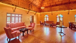 A spacious room with wooden ceiling beams, a chandelier, and a large window with a view.