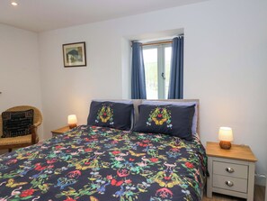 Ein Schlafzimmer mit einem Bett, zwei Nachttischen, einem Sessel, einem Fenster mit Vorhängen und einem Wandbild.