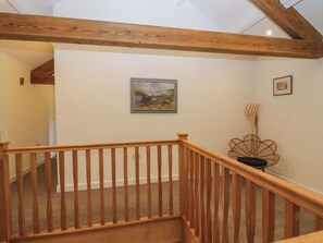 A wooden staircase with a railing, a framed landscape painting on the wall, and a rustic chair. - High Birks Barn (Sedbergh)