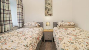 A bedroom with two beds, a nightstand, a lamp, a painting on the wall, and plaid curtains. - High Birks Barn (Sedbergh)