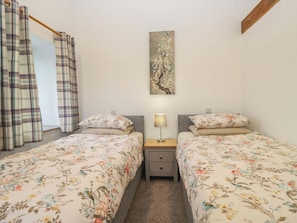 A bedroom with two beds, a nightstand, a lamp, a painting on the wall, and plaid curtains. - High Birks Barn (Sedbergh)