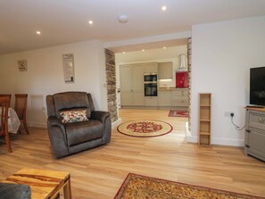 A living room with a leather armchair, a wooden coffee table, and a patterned rug. - High Birks Barn (Sedbergh)