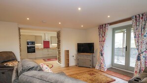 A living room with a grey sofa, a television, and a kitchen in the background. - High Birks Barn (Sedbergh)