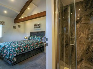 A bedroom with a bed, a nightstand, a wall-mounted lamp, a framed picture, and a glass shower enclosure. - High Birks Barn (Sedbergh)