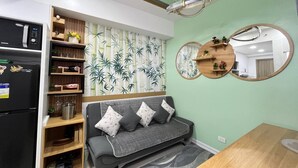 A compact living space with a sofa, a dining table, a refrigerator, and a wall-mounted mirror. - Sunset View 3-Bedroom SMDC (Pasay)
