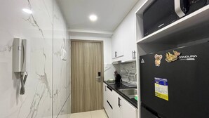 A compact kitchen with white cabinets, a black refrigerator, and a wooden door. - Sunset View 3-Bedroom SMDC (Pasay)