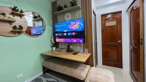 A living room with a TV, wooden shelves, a bench, and a door. - Sunset View 3-Bedroom SMDC (Pasay)