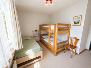 Ein Zimmer mit einem Etagenbett, einem Einzelbett, einem Sessel, einem kleinen Tisch mit einer Pflanze und einem gerahmten Bild an der Wand.