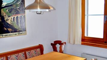 Un coin repas avec une table et des chaises en bois, un luminaire suspendu, une fenêtre avec des rideaux et un tableau accroché au mur.