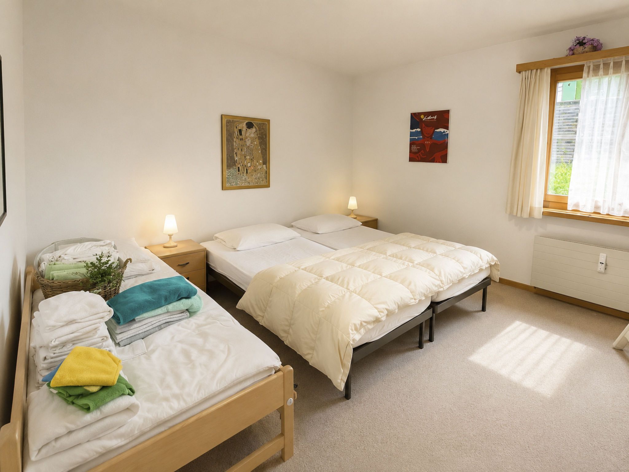 Un dormitorio con dos camas individuales, una cama más grande, una mesita de noche con lámpara, un cuadro en la pared, una ventana con cortinas y un radiador.