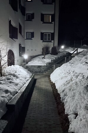 Ein verschneiter Weg führt zu einem Gebäude mit vielen Fenstern und einer Backsteinmauer.
