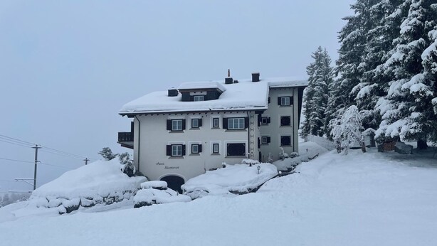 Um edifício de vários andares com telhado coberto de neve e uma placa com a inscrição 'Chasa Rieseant'.