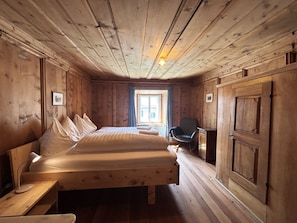 Ein Zimmer mit Holzboden, einem Bett, einem Sessel, einem Schreibtisch und einem Kleiderschrank.