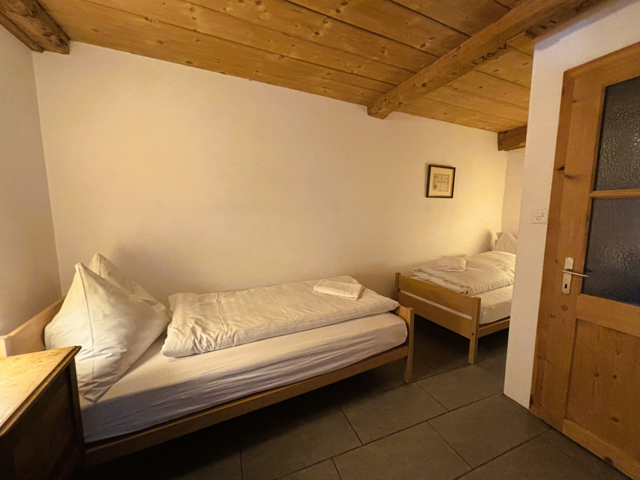 Un petit logement composé d’une seule pièce, avec un plafond en bois, un lit, une table de chevet et une porte.