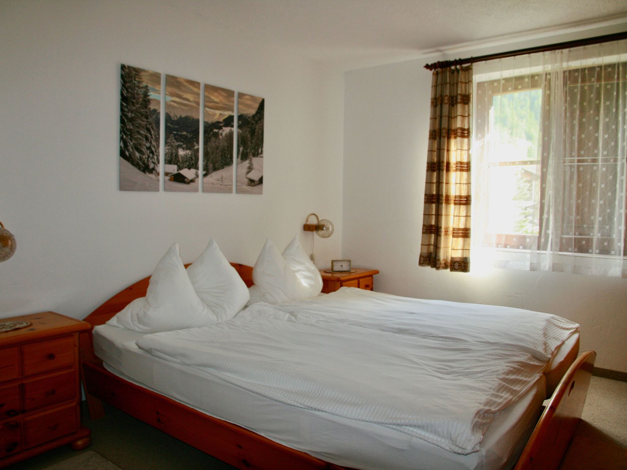 Un dormitorio con una cama, una mesita de noche, un reloj de pared y una ventana con cortinas.