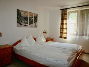 Ein Schlafzimmer mit einem Bett, einem Nachttisch, einer Wanduhr und einem Fenster mit Vorhängen.