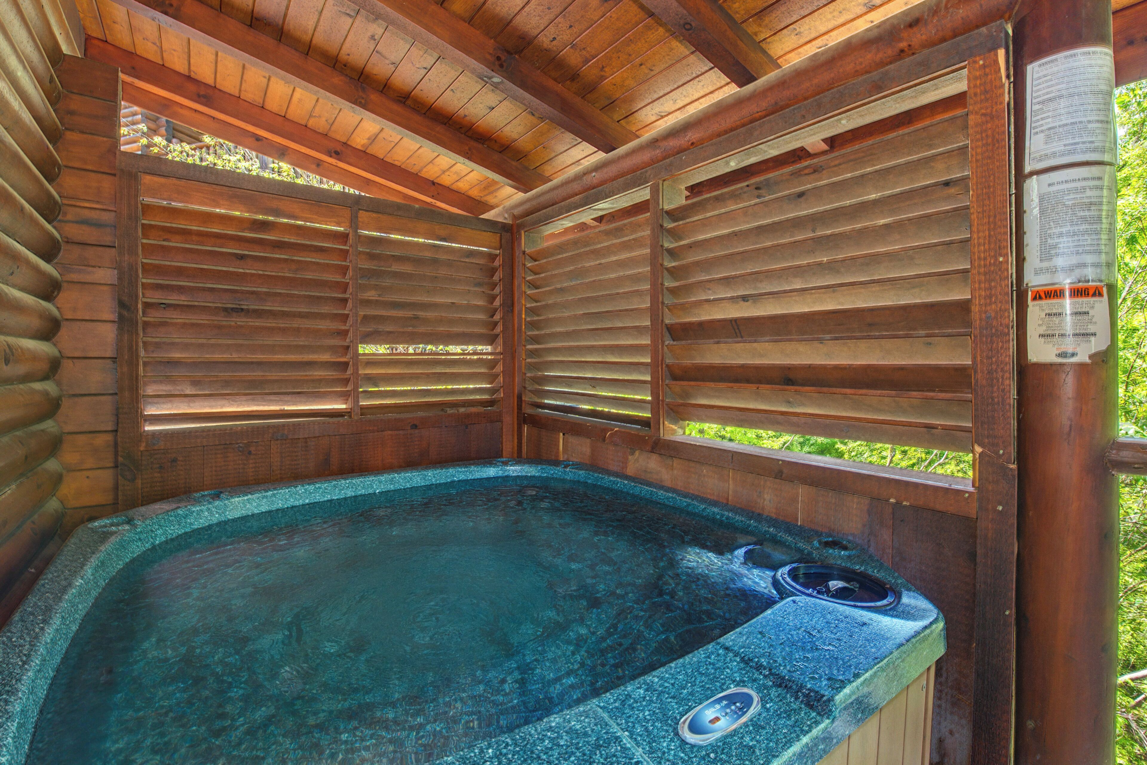 Une cabane en bois dotée d’un bain à remous, de lambris en bois aux murs et d’une fenêtre donnant sur un paysage verdoyant.