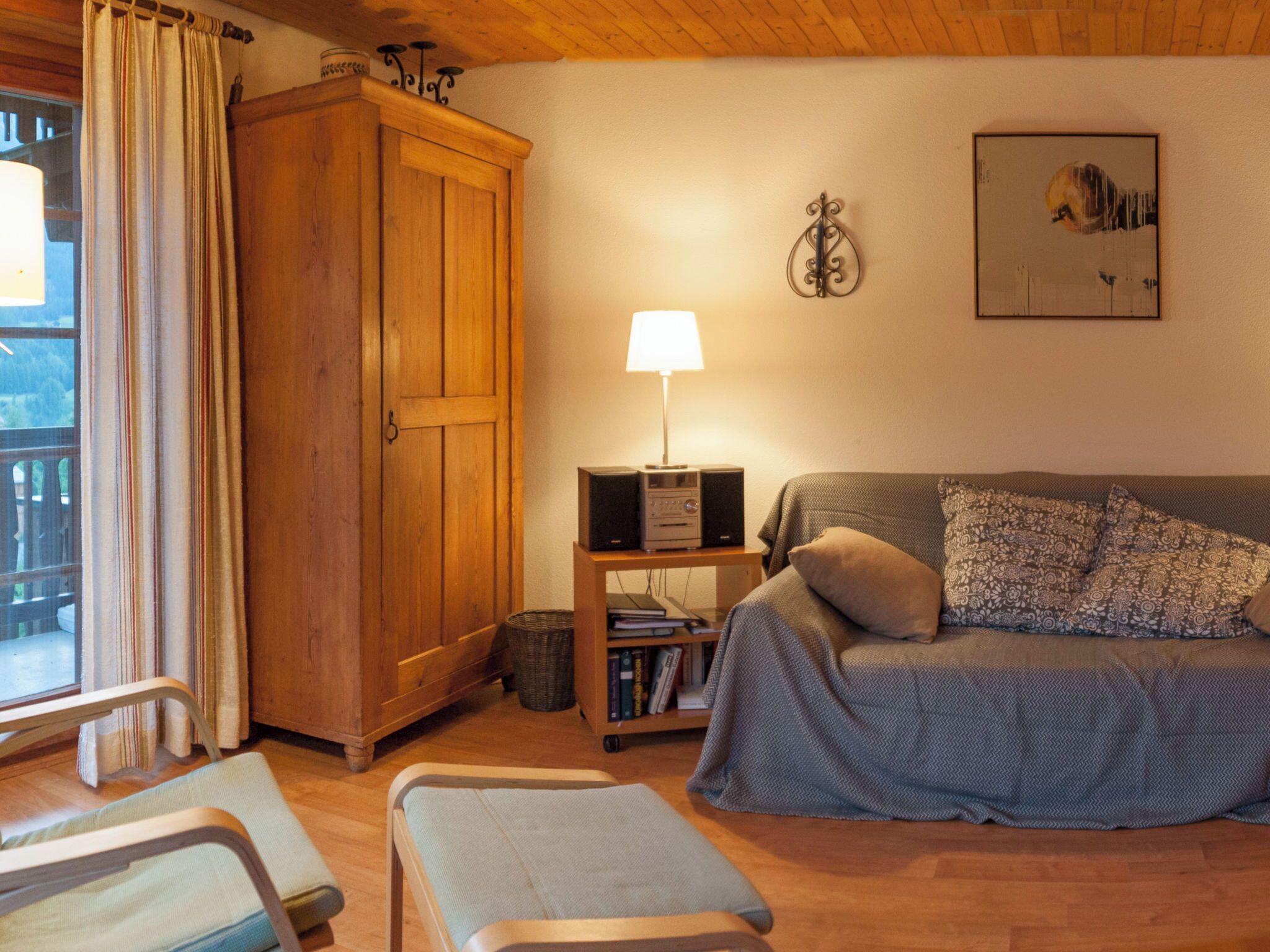 Une pièce chaleureuse avec une armoire en bois, un téléviseur posé sur une petite table, un canapé agrémenté de coussins à motifs et une fenêtre avec des rideaux.